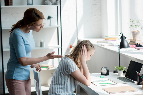 Depressed teen daughter sitting at desk while her mother yelling at her.