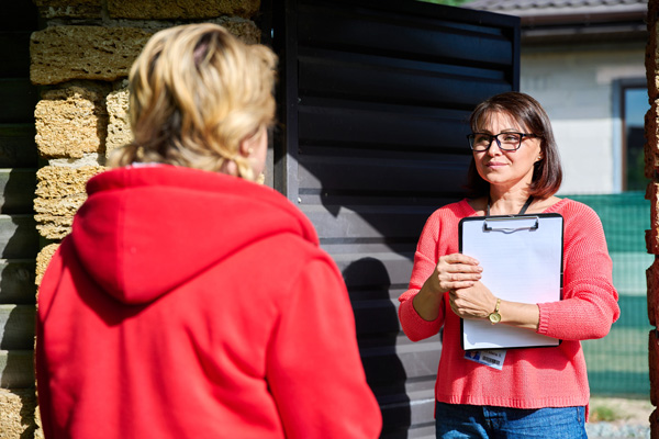 Female social worker talking to a mature woman near gate of house.